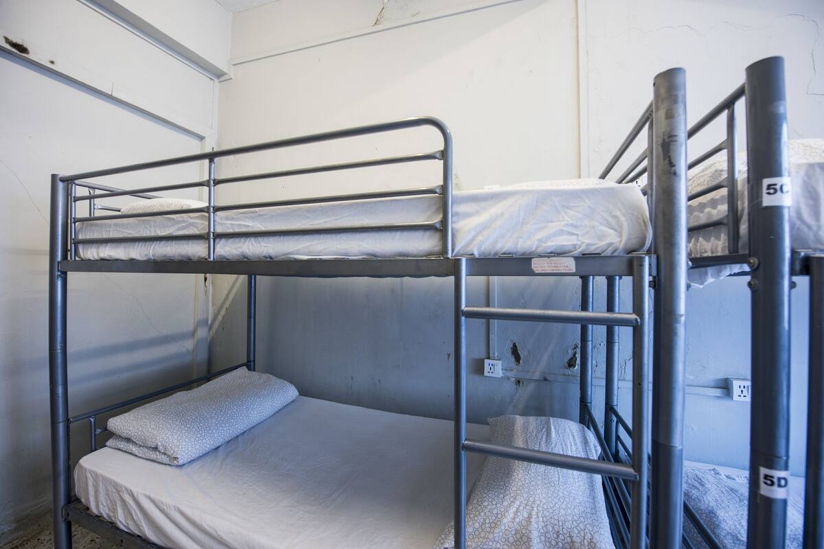 Une chambre avec un lit superposé, dotée de barrières métalliques et de draps blancs.