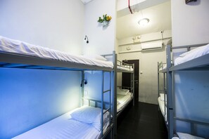 A narrow corridor with bunk beds on either side, a small plant on the wall, and an air conditioning unit above. - Urban Hostel (Singapore)