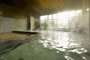 A hot spring area with a stone wall, a wooden ceiling, and a large window allowing natural light. - Hotel Ryutouen (Saga)