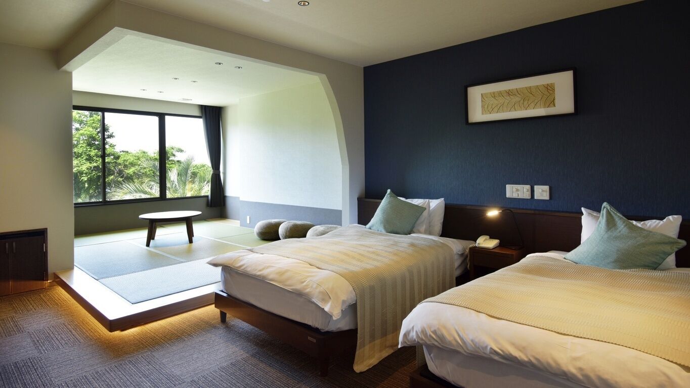 A modern hotel room with two beds, a large window, and a view of greenery.