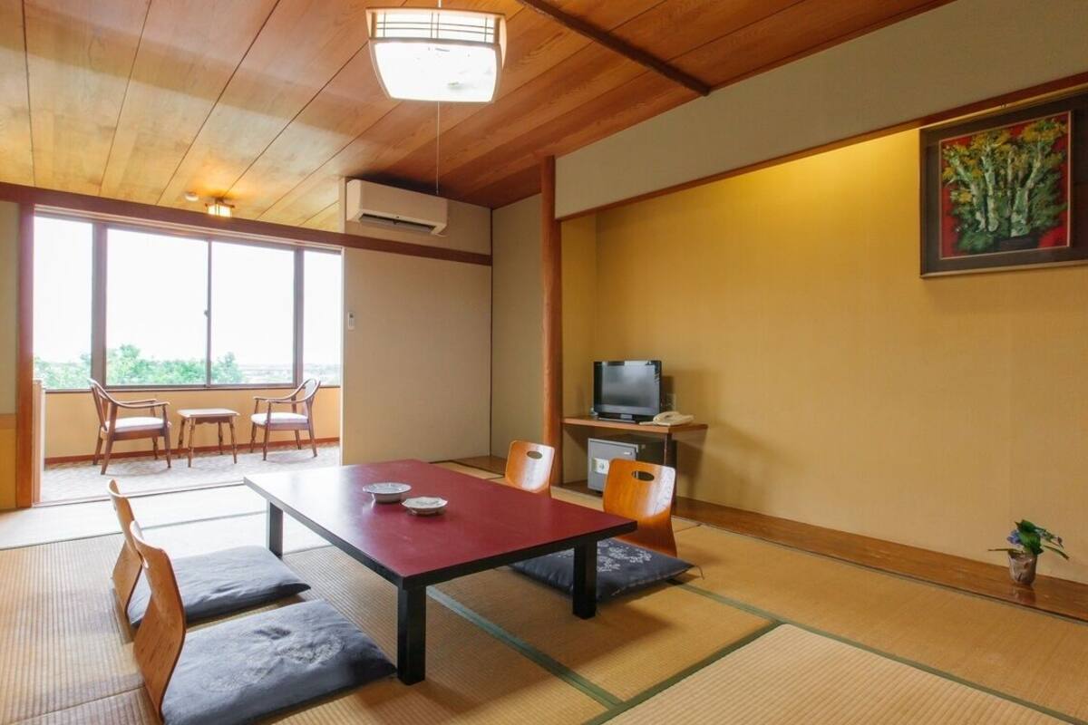 A traditional Japanese room with tatami flooring, a low table with cushions, a television, and a painting on the wall.