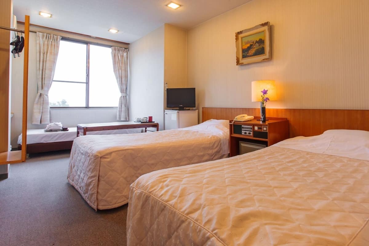 A hotel room with two beds, a TV, a desk, and a window with curtains.