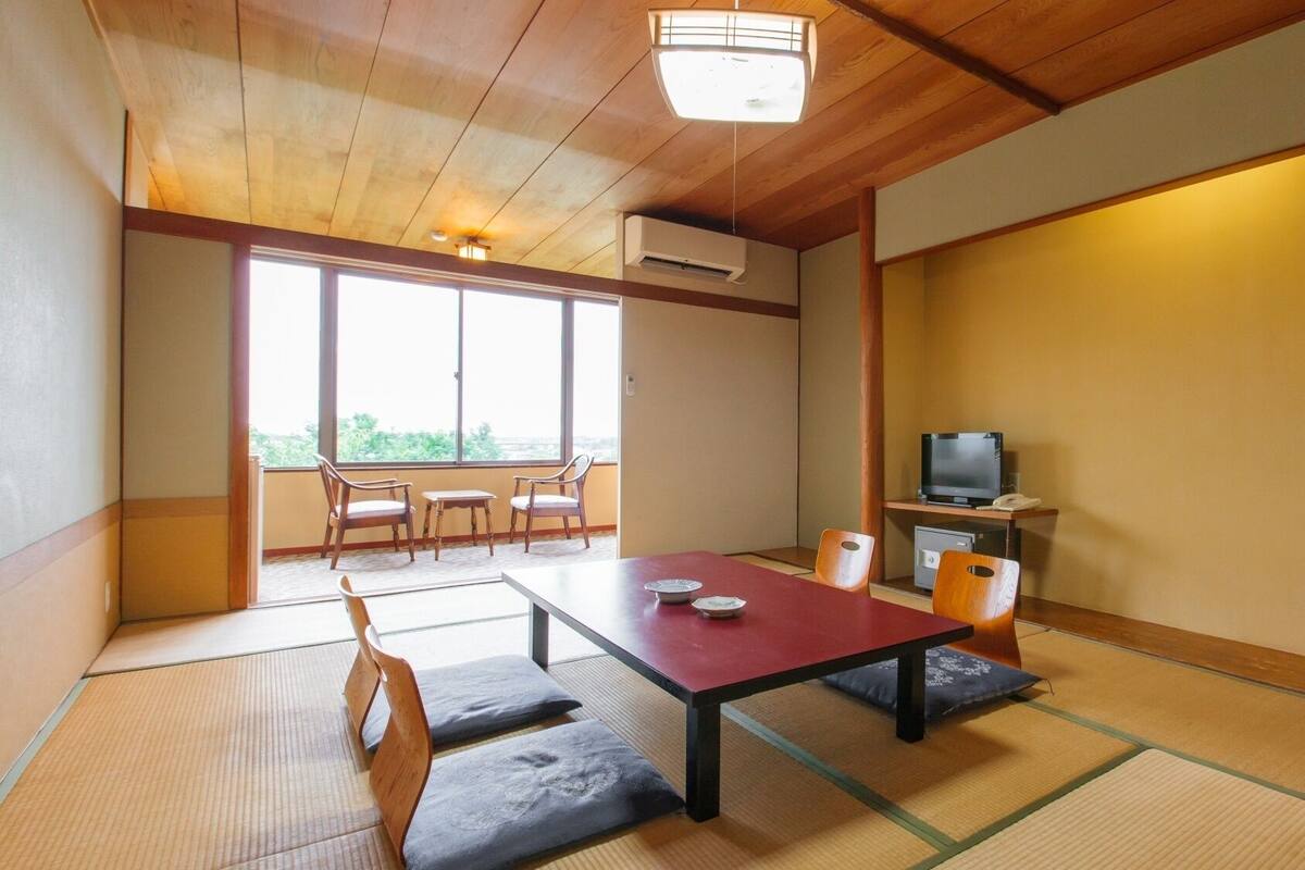 A traditional Japanese room with tatami flooring, a low table with cushions, a television, and a painting on the wall.