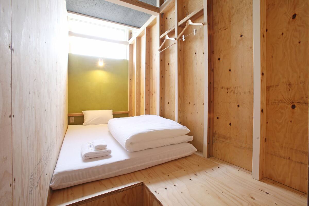 Ein kleiner, hölzerner Raum mit einem Bett, einem Schrank aus Holz und einem Fenster mit Tageslicht.