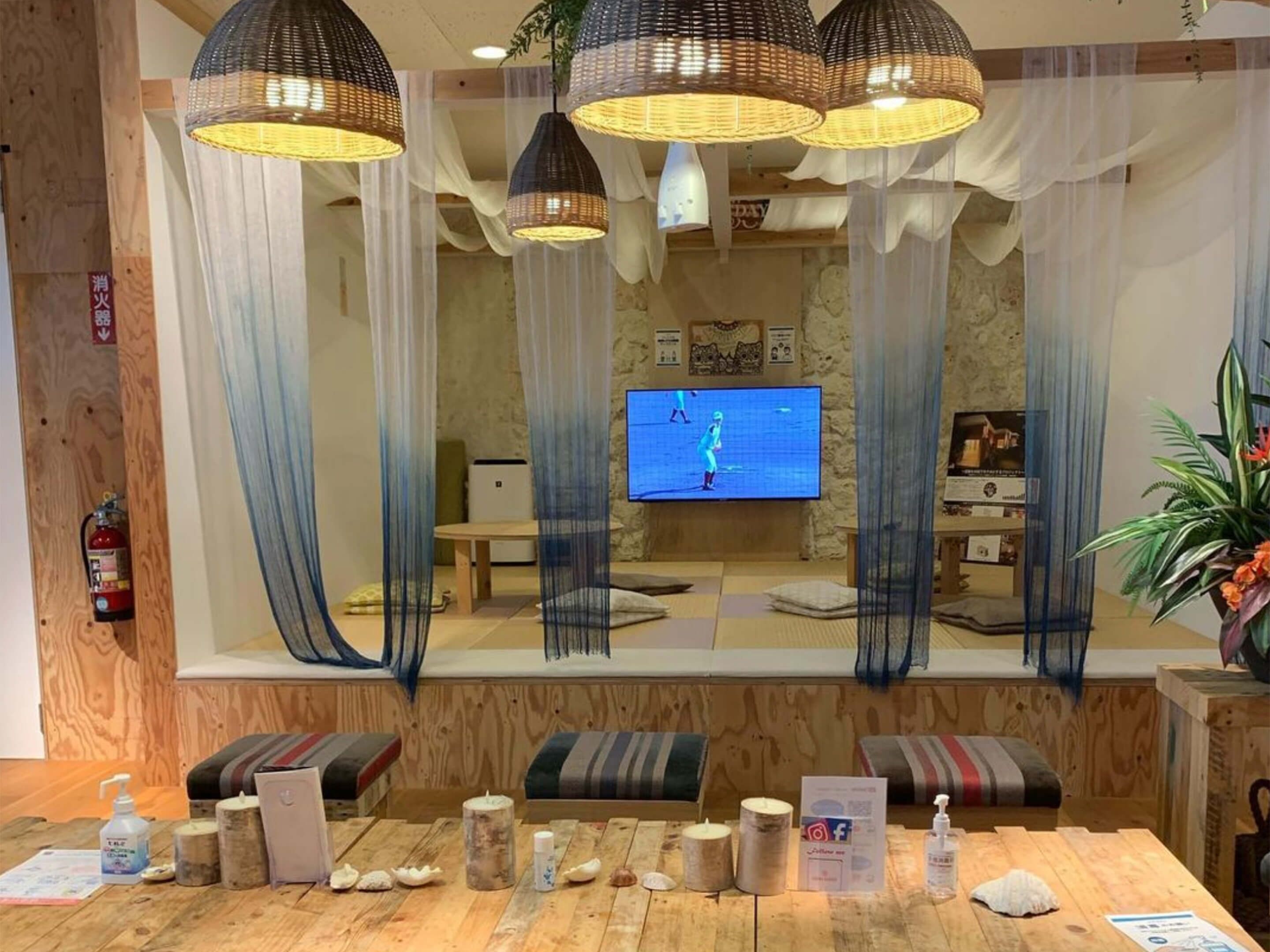 Ein Zimmer mit Holzboden, einer Holzeinchecktheke, einem Fernseher an der Wand und einem großen Fenster mit durchsichtigen Vorhängen.