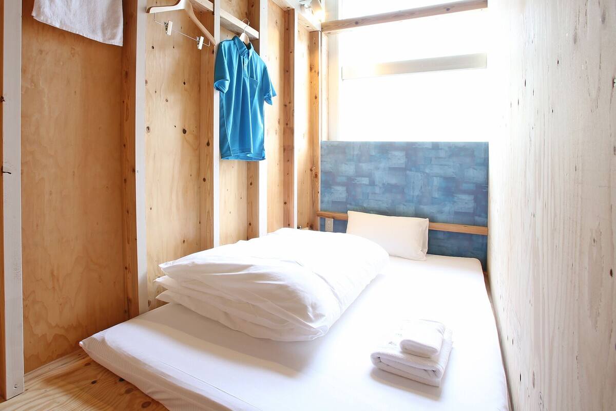 Ein Zimmer mit Holzboden, einem Bett, einem Haken zur Handtuchaufhängung und einem blauen Handtuch.