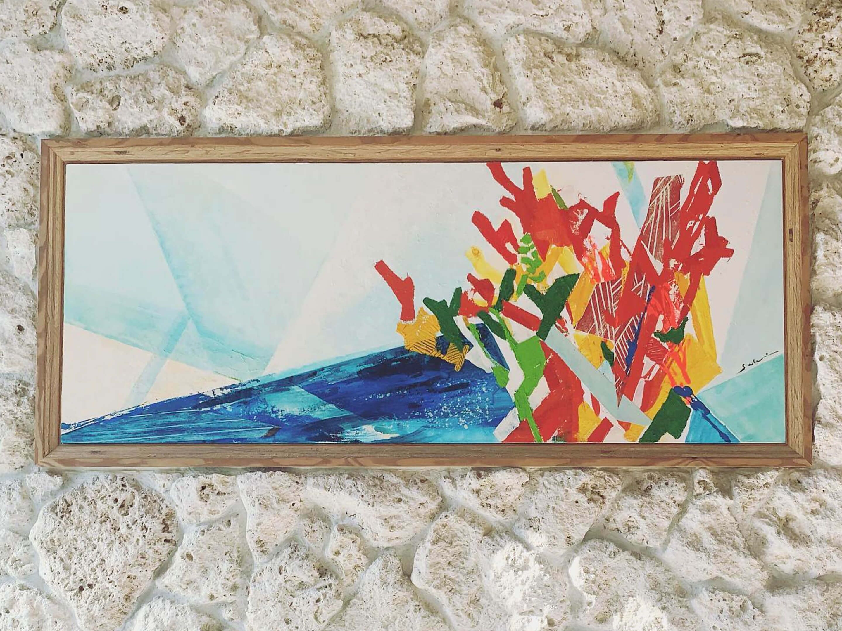 Ein gerahmtes, abstraktes Gemälde mit geometrischen Formen und leuchtenden Farben, an einer strukturierten Wand angebracht.