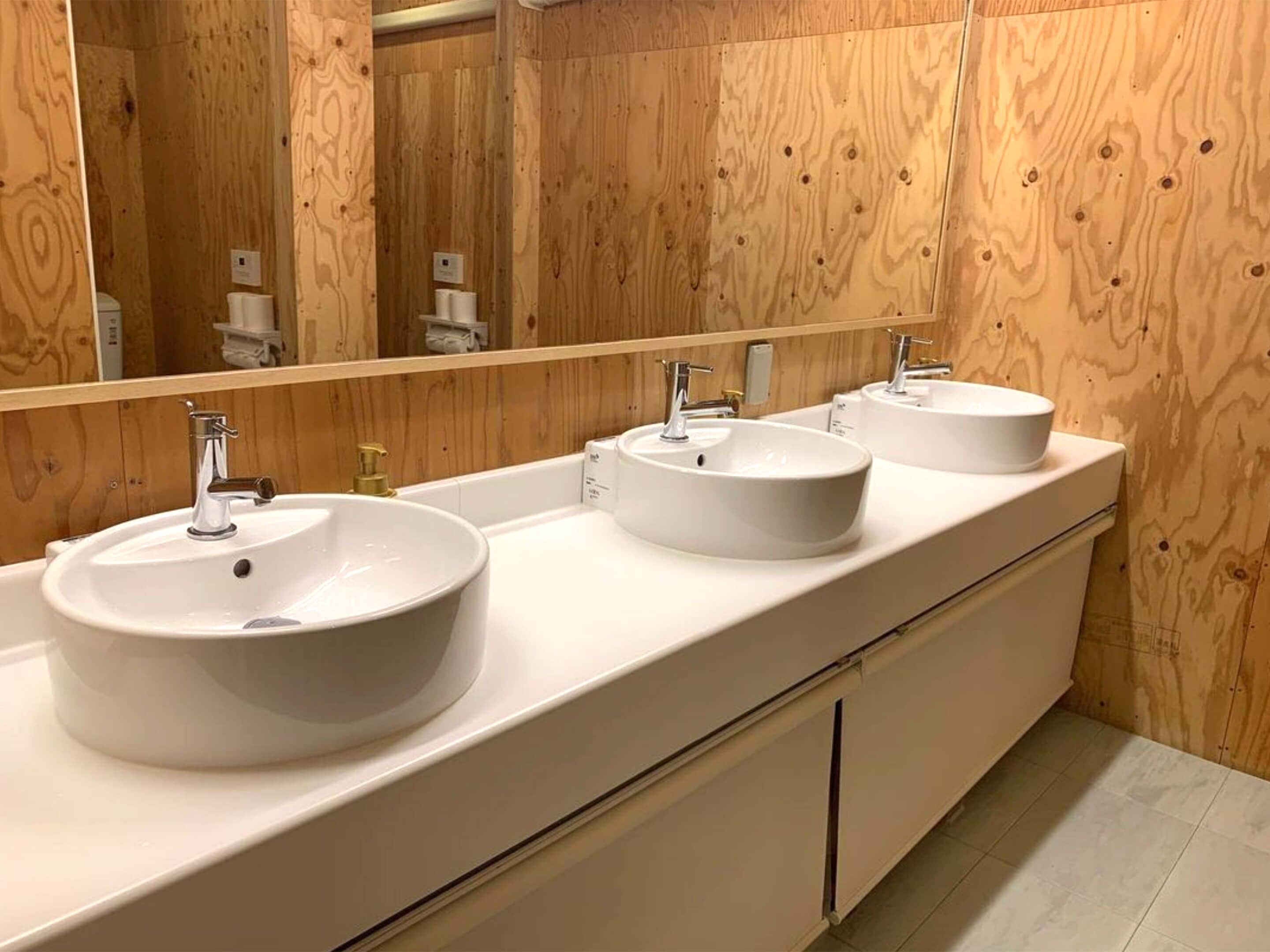 A bathroom with three white sinks, a large mirror, and wooden paneling on the walls.