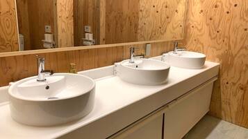 Een badkamer met drie witte wasbakken, een grote spiegel en houten lambrisering.