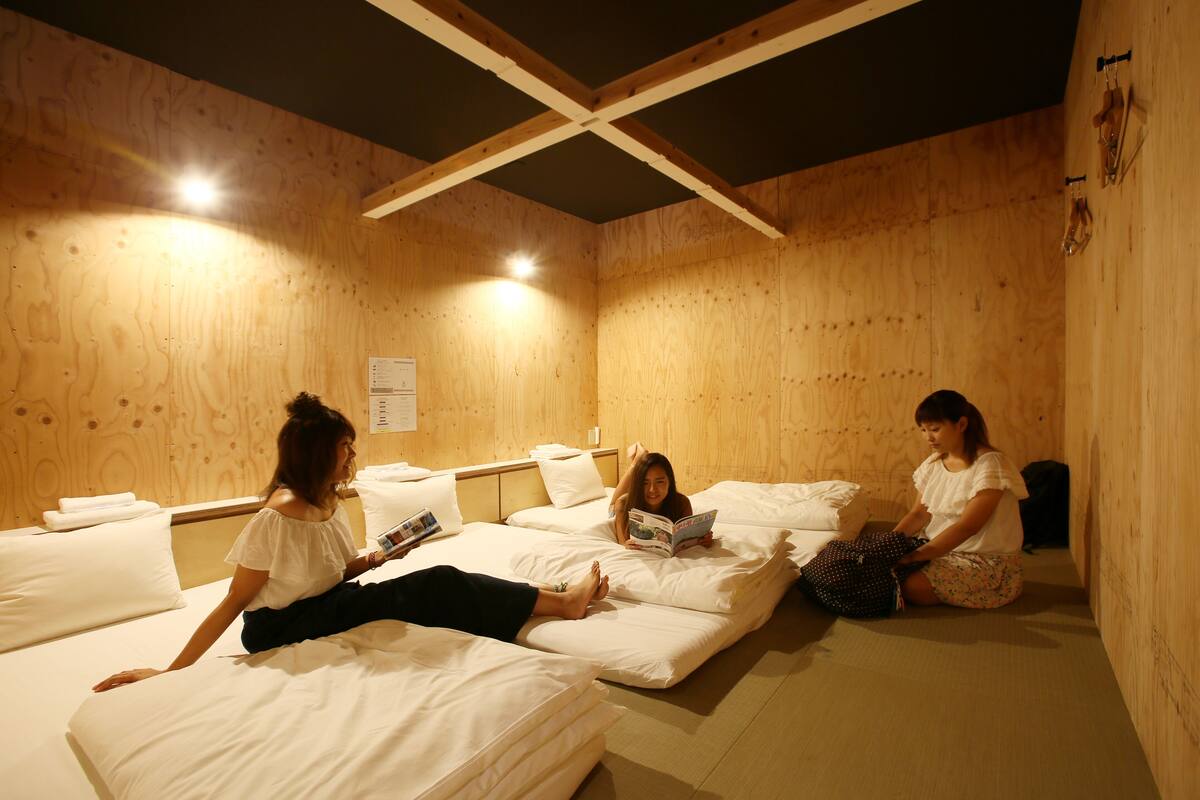Ein Zimmer mit Holzwänden und -decke, mehreren Betten mit weißer Bettwäsche und einem Bulletinboard an der Wand.