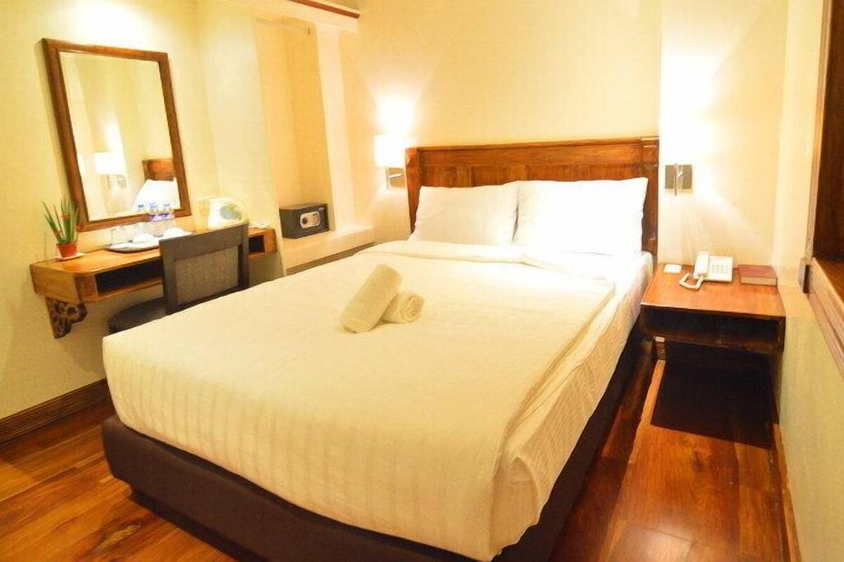 A neatly made bed with pillows, a bedside table with a lamp, a mirror, and a small plant.