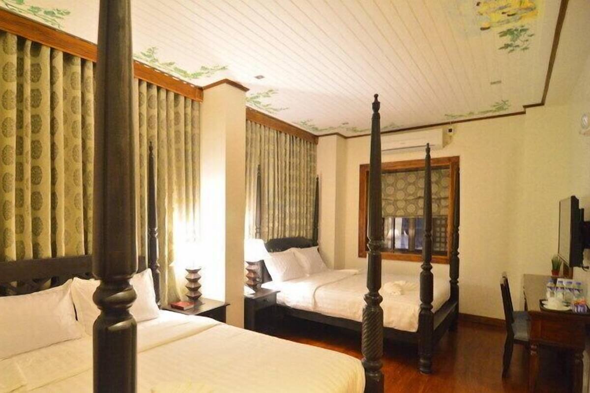 A traditional four-poster bed with a wooden headboard and footboard, a bedside table, and a window with curtains.