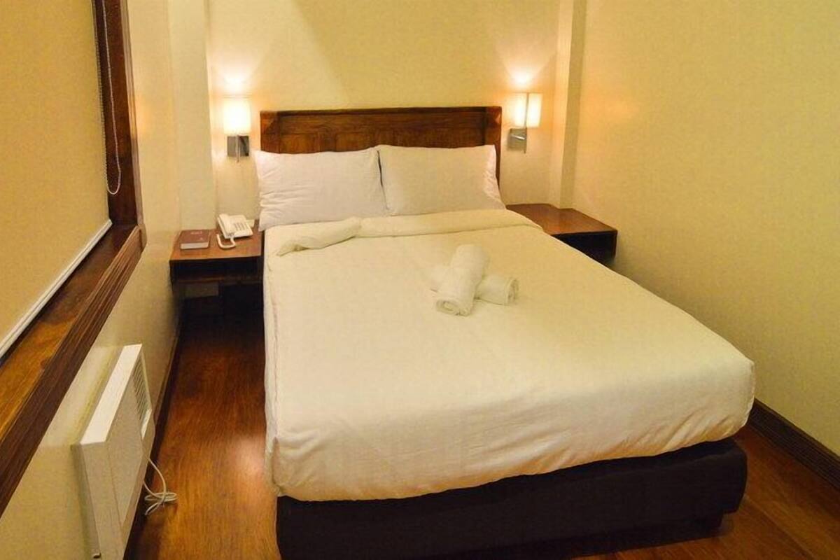 A hotel room with a wooden headboard, a bedside table with a lamp, and a neatly made bed with towels.