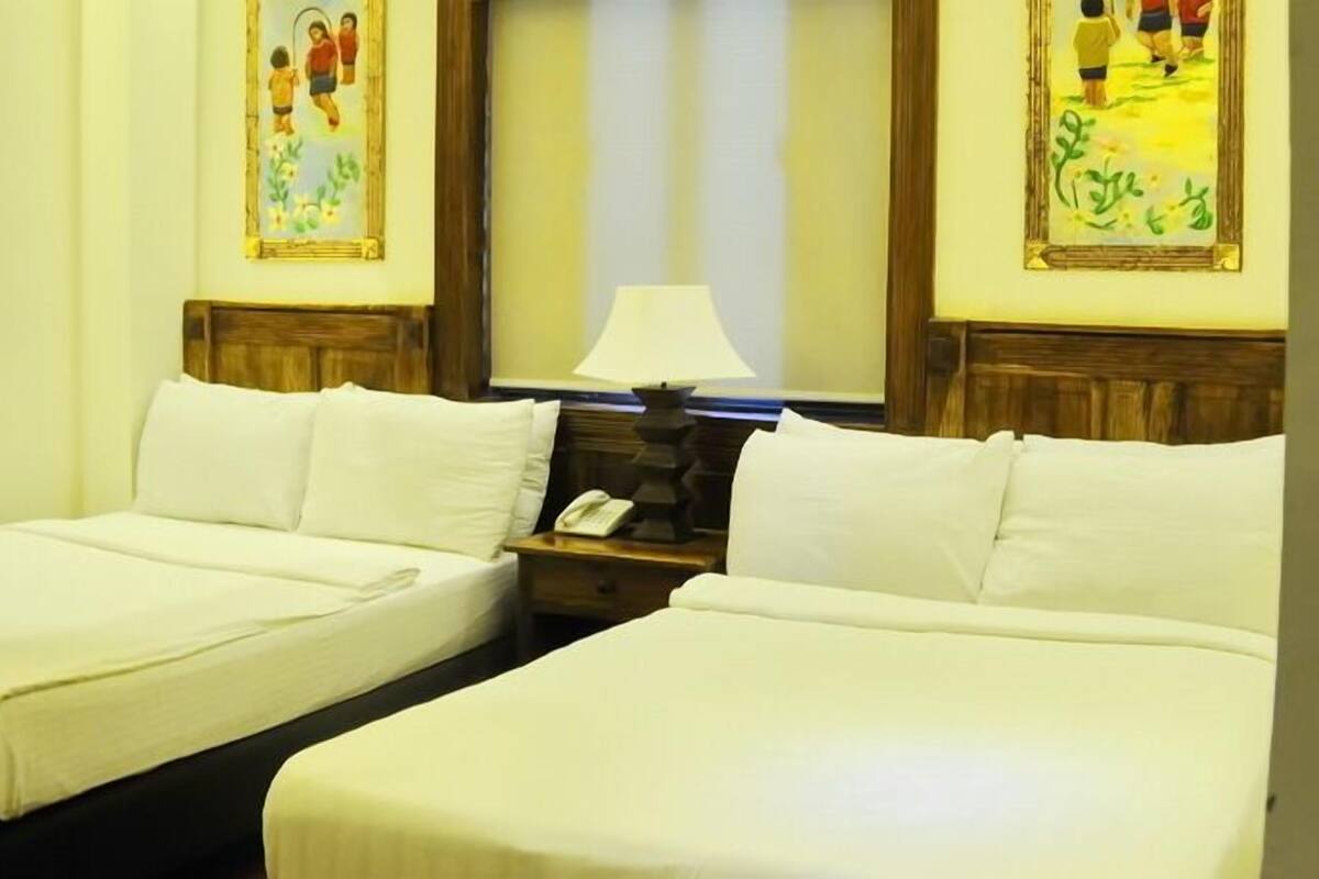 A hotel room with two single beds, a nightstand with a lamp, and two framed pictures on the walls.