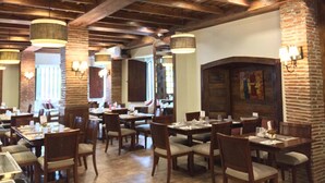 A restaurant with wooden beams and brick walls, featuring tables and chairs set for dining.