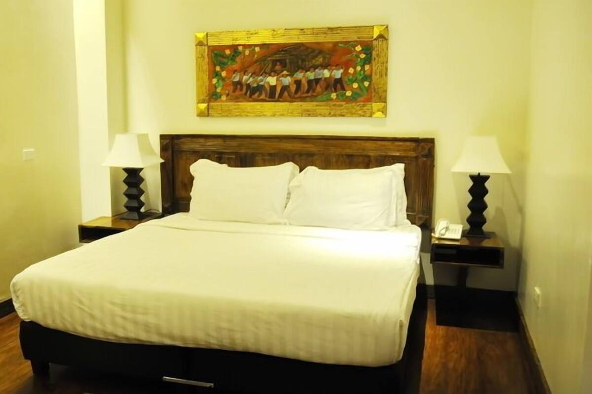 A neatly made bed with white linens, a wooden headboard, and two bedside lamps.