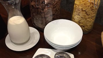 A table with a pitcher of milk, two jars of cereal, and a stack of white plates.