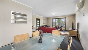 A modern living room with a glass dining table, red sofa, and a TV on a wooden stand.