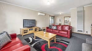 A living room with a red leather sofa, a wooden coffee table, a flat-screen TV, and a modern air conditioning unit.