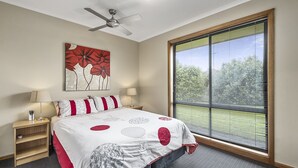 A bedroom with a bed, a nightstand, a ceiling fan, a window with blinds, and a wall art piece.