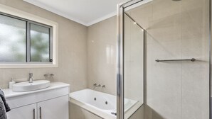 A modern bathroom with a glass-enclosed shower, a white sink, and a large mirror above the vanity. - Megan Court Apartments (Mount Gambier)