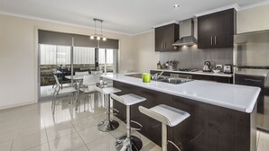 A modern kitchen with a central island, bar stools, stainless steel appliances, and a view to the outdoors. - Megan Court Apartments (Mount Gambier)