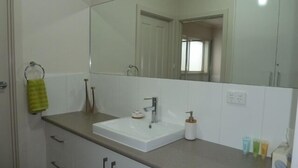 A bathroom with a white sink, a mirror, and a towel rack. - Hart Street Apartment (Mount Gambier)