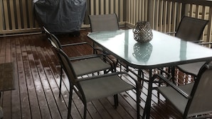 An outdoor patio with a glass table and metal chairs, a covered grill, and a decorative lantern. - Hart Street Apartment (Mount Gambier)