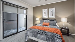 A bedroom with a bed, two bedside lamps, a ceiling fan, and a sliding glass door. - MG Delux Apartment (Mount Gambier)