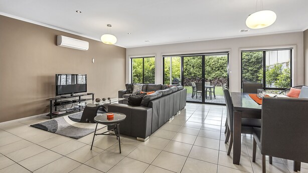 A modern living room with a sofa, TV, dining table, and chairs. - MG Delux Apartment (Mount Gambier)