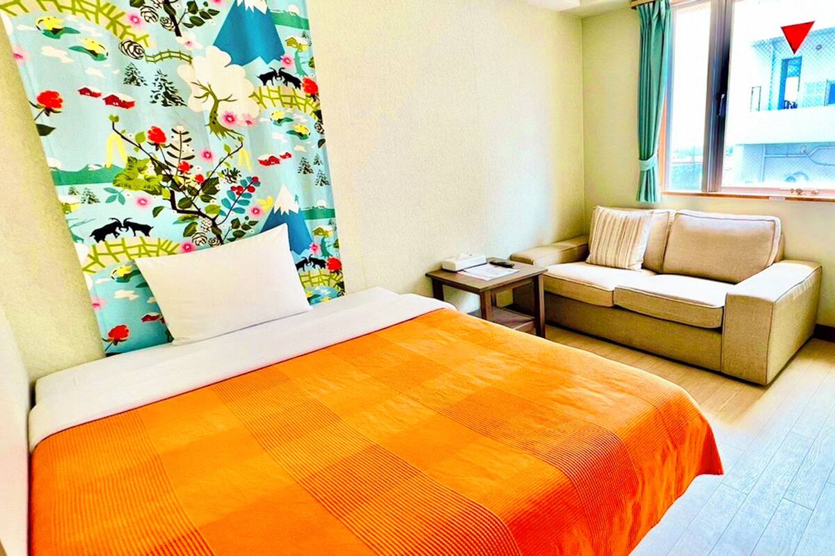 Una habitación de hotel con cama, sofá, una mesita, lámpara y minibar.