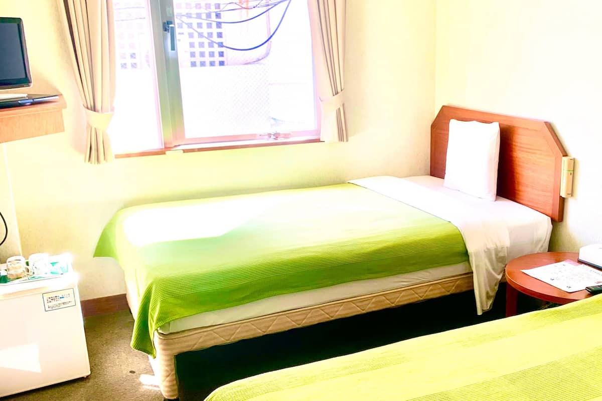 Habitación de hotel con dos camas, una mesita, televisor y ventana con cortinas.