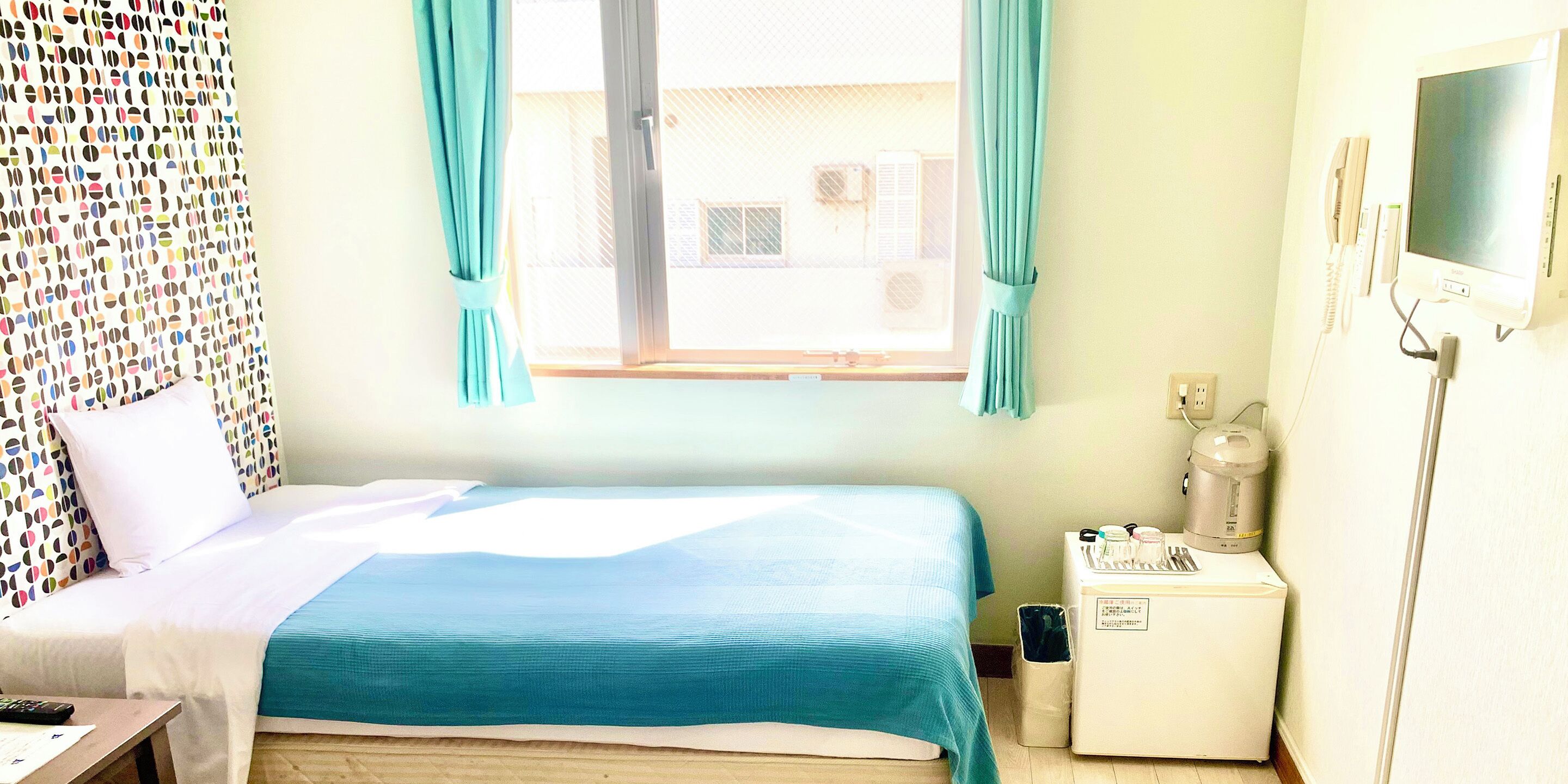 A hotel room with a bed, a small bedside table, a TV, and a window with curtains.