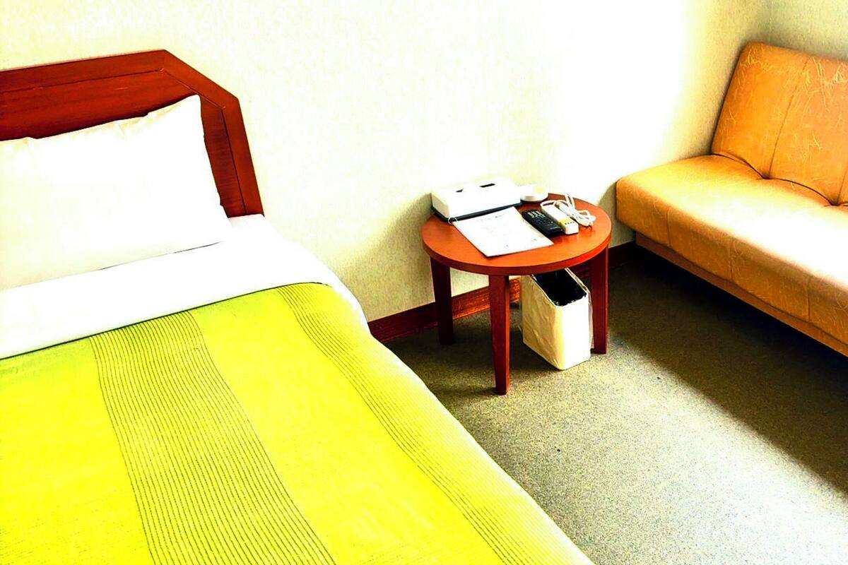 Una habitación de hotel con cama, una mesita redonda con un teléfono y papeles, y un sofá.