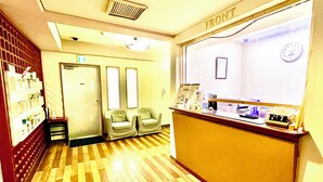 A reception area with a counter, two armchairs, a clock, and a framed picture on the wall. - Hotel Happy Holiday Ishigakijima (Ishigaki)