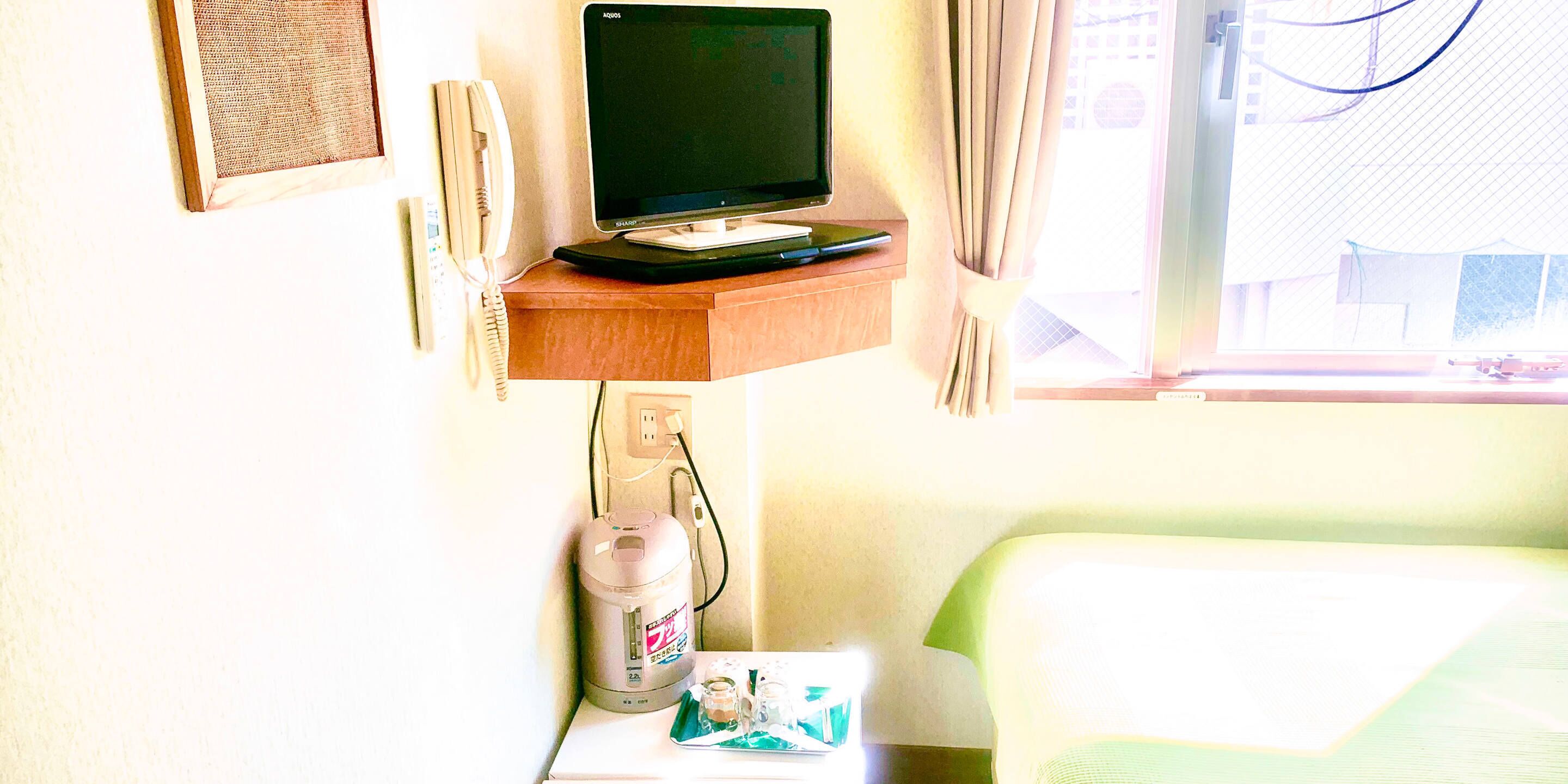 Ein Hotelzimmer mit Fernseher auf einer Holzablage, einem Wasserkocher und einem kleinen Tisch mit Tasse und Untertasse.