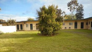 A building with a flat roof, a small tree in the center, and a well-maintained lawn. - Rankins Springs Motel (Rankins Springs)