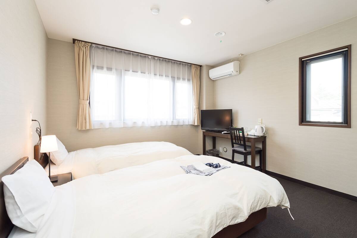 Een hotelkamer met twee bedden, een bureau met televisie en een raam met gordijnen.
