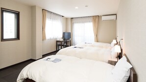 Habitación de hotel con dos camas, un escritorio y un televisor, además de un equipo de aire acondicionado en la pared.
