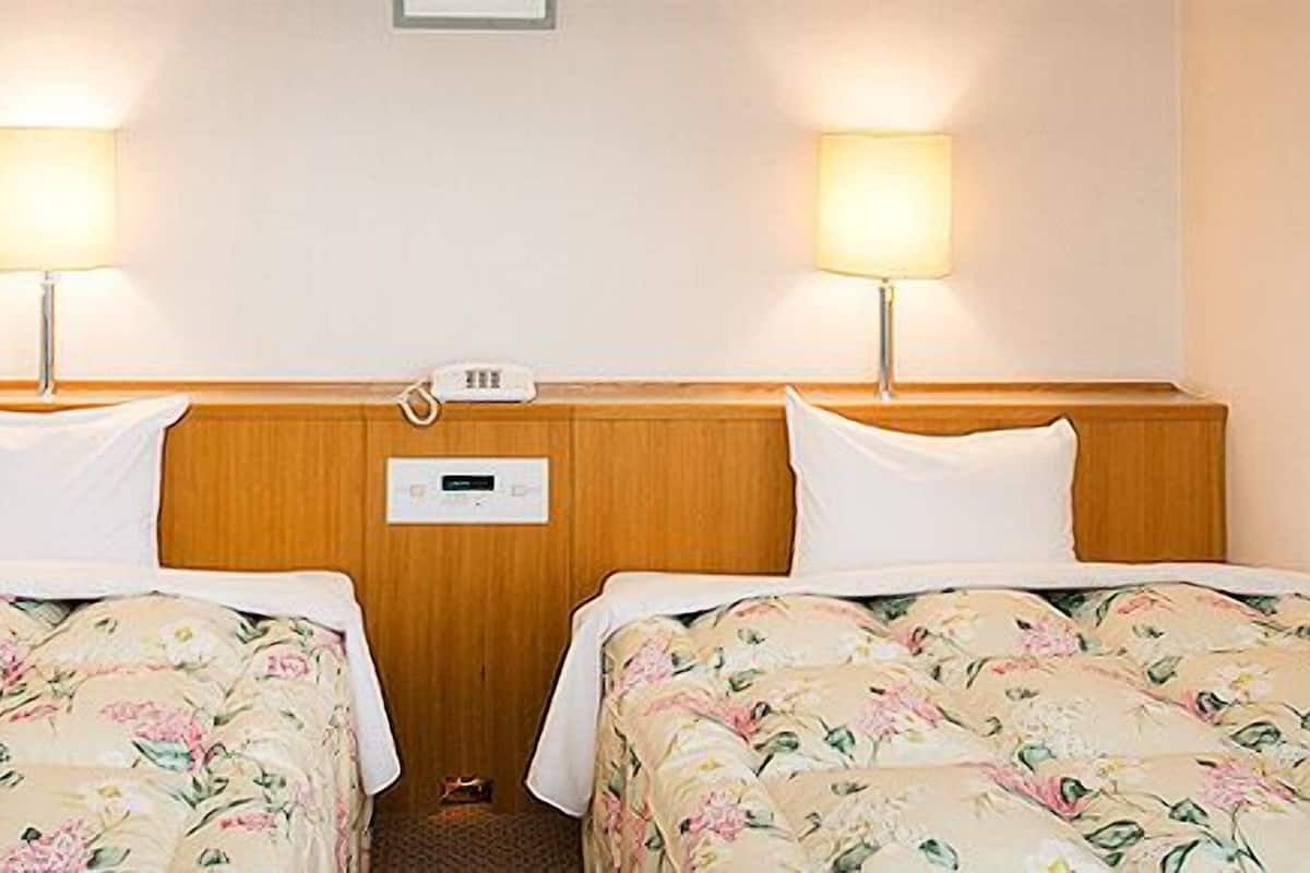 A hotel room with two single beds, each with floral bedding, a wooden headboard, bedside lamps, and a control panel on the wall.