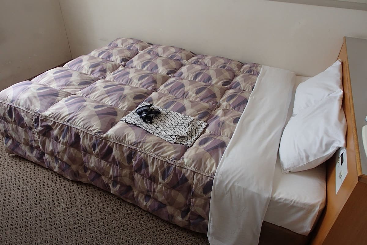 A single bed with a patterned duvet, a white pillow, and a small decorative pillow on the bed.