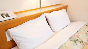 A hotel room with a wooden headboard, a white telephone, and a floral bedspread. - Hotel Shinsuien (Nagoya)