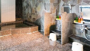A bathroom with a stone wall, a bathtub, and a shower area. - Hotel Shinsuien (Nagoya)