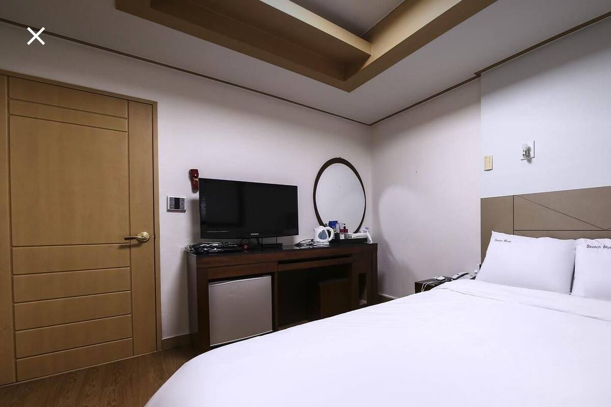 A hotel room with a bed, a desk with a TV, a mirror, and a small fridge.