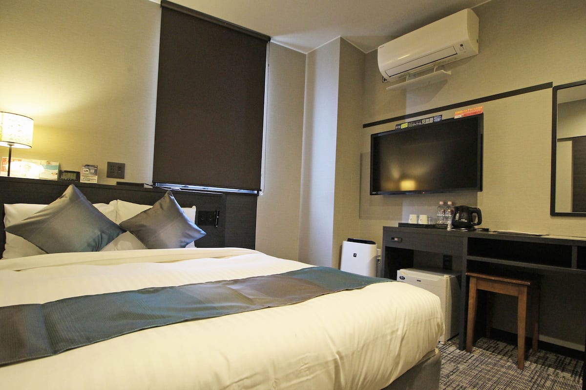 A hotel room with a large bed, a desk, a flat-screen TV, an air conditioner, and a coffee maker.