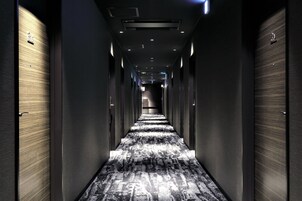 Un largo y estrecho pasillo de hotel con puertas a ambos lados y una alfombra estampada.