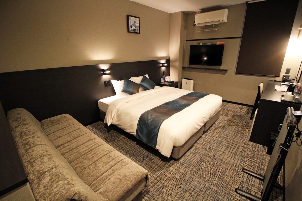 A hotel room with a bed, a sofa, a desk with a computer, and a TV.