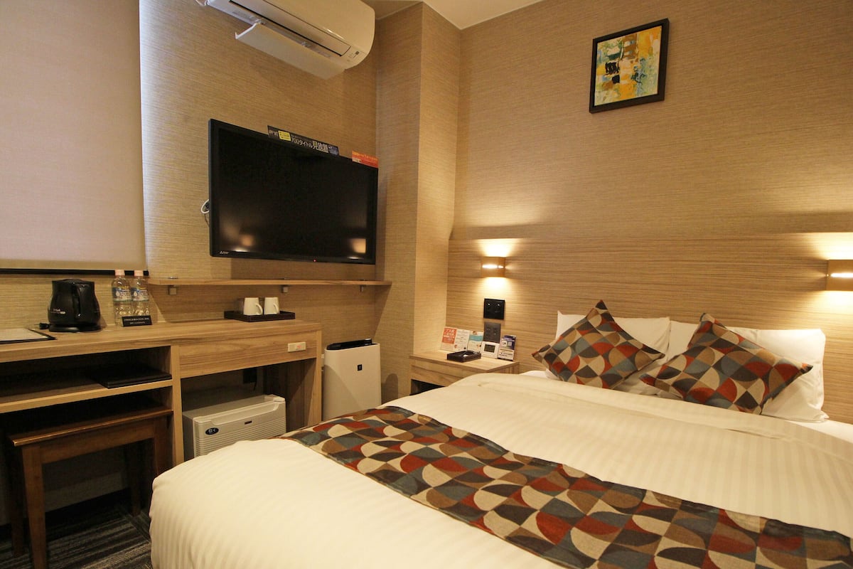 A hotel room with a bed, a desk, a television, and a minibar.