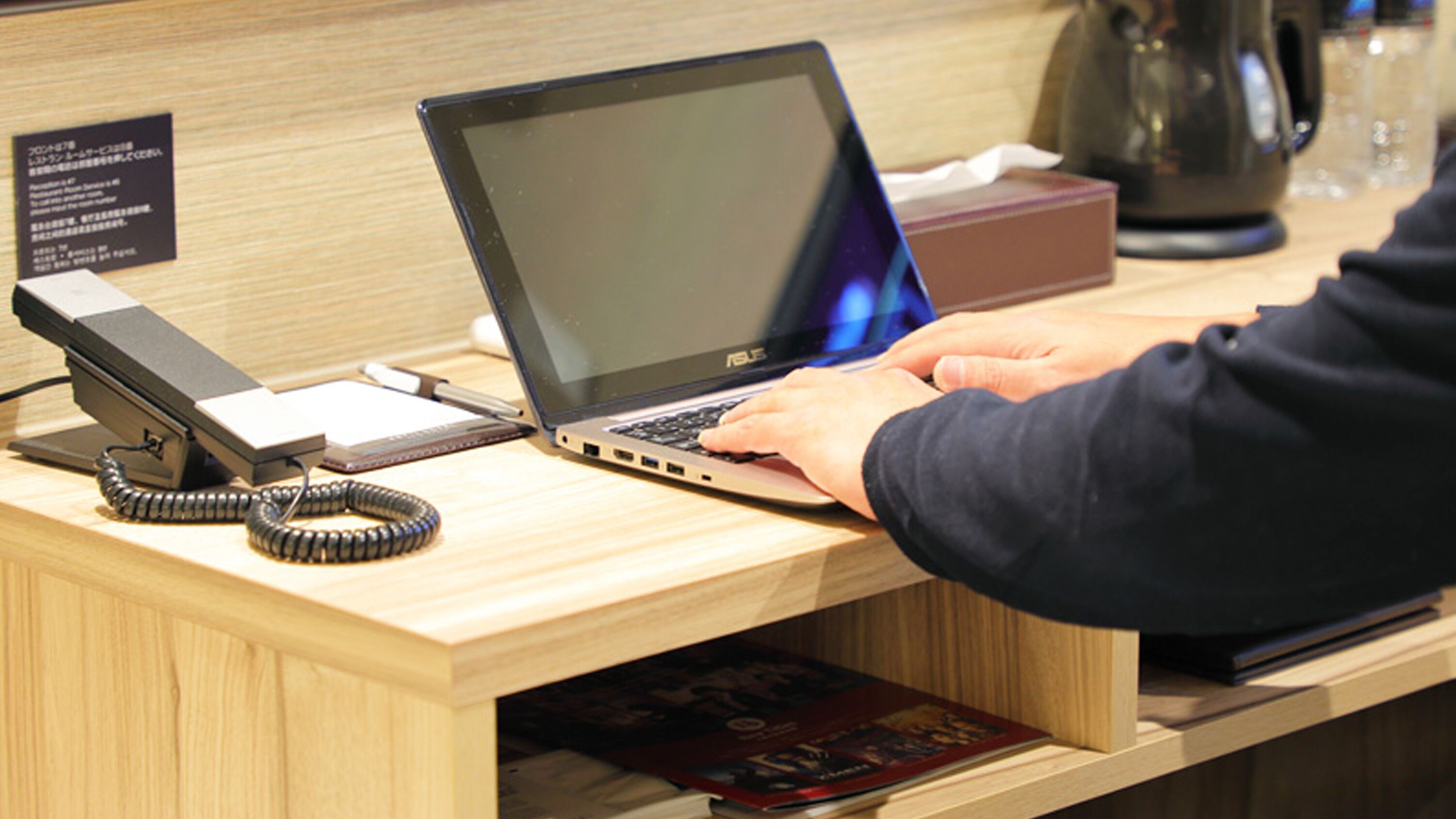 Un mostrador de recepción de madera con una computadora portátil, un teléfono y una caja.