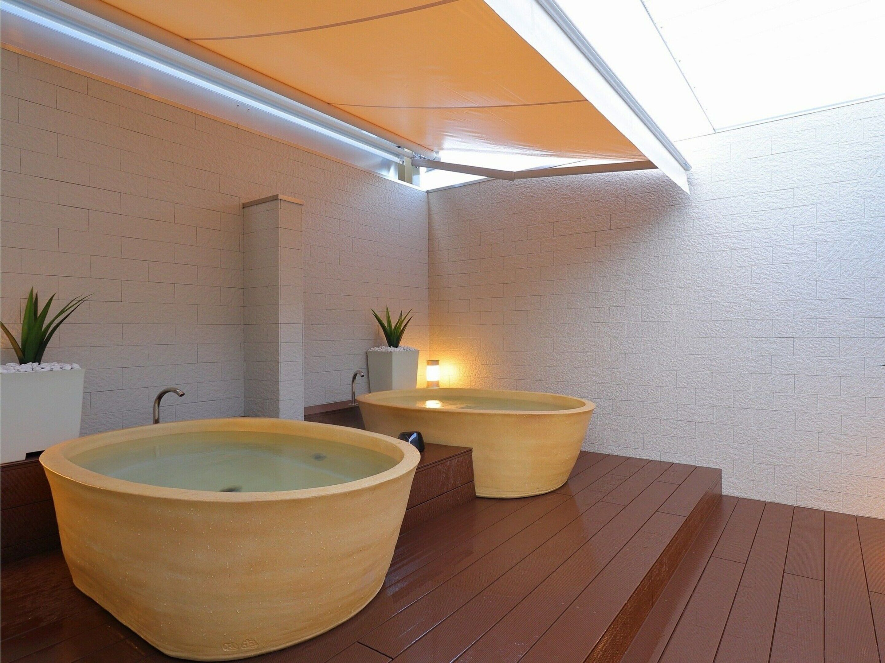 A spa area with two large tubs, wooden flooring, white brick walls, and a skylight.